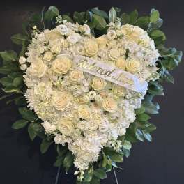 Heart-shaped white floral wreath with a ribbon reading "Beloved Mom"