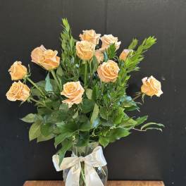 Peach roses arranged in a clear glass vase with a white ribbon.
