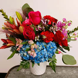 Colorful mixed bouquet in a white vase with blue hydrangeas and red roses