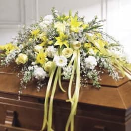 Yellow and white floral spray on a casket with long ribbon streamers