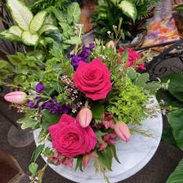 Low arrangement of hot pink roses, tulips, and mixed blooms in a white vase on a small round table