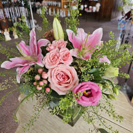 Pink lilies, roses, and lisianthus arranged in a clear glass cube vase