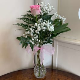 Pink rose in a clear vase with white baby's breath and a pink ribbon
