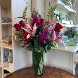 Tall bouquet of red roses and pink lilies in a green glass vase