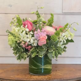 Pink and white mixed flower arrangement in a clear glass cylinder vase lined with green leaves