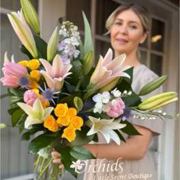 Large bouquet of lilies, roses, and small white flowers in a glass vase
