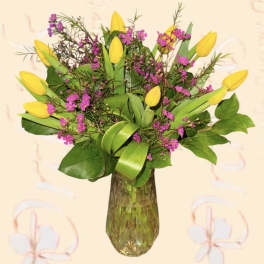 Yellow tulips and pink filler flowers in a glass vase