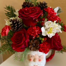 Red roses and carnations arranged in a Santa mug with pinecones.