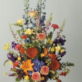 Tall mixed bouquet in a pale vase with roses, lilies, and blue flowers