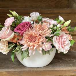 Pink and peach mixed flower arrangement in a white bowl vase