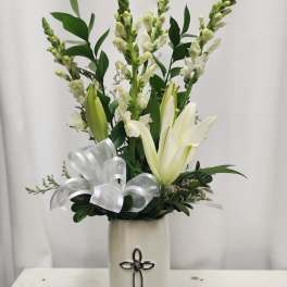 White lilies and snapdragons in a tall vase with a silver ribbon bow