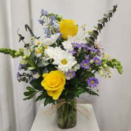 Bouquet of yellow roses, white daisies, and purple asters in a glass vase