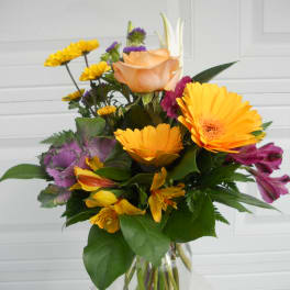 Mixed bouquet in a clear glass vase with orange, yellow, and purple flowers