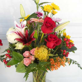 Mixed bouquet of red roses, lilies, and yellow flowers in a glass vase
