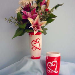 Pink lilies and white daisies in a tall heart-decorated vase with a matching cup