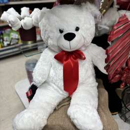 White teddy bear with a red ribbon sitting among gift items