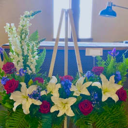 Floral arrangement with white lilies, red roses, and purple blooms on an easel
