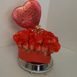 Heart-shaped balloon above a box of red roses on a mirrored base