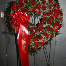 Heart-shaped red rose wreath on a stand with a red ribbon