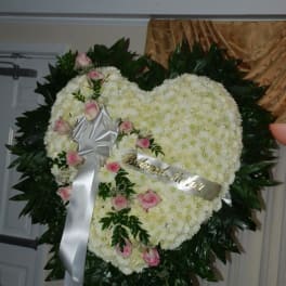 Heart-shaped white floral wreath with pink roses and a silver ribbon