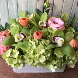 Mixed floral arrangement in a white rectangular container with pink and green blooms