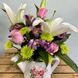 Pink and white flowers arranged in a white teapot vase