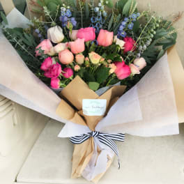 Bouquet of pink and blue flowers wrapped in paper with a striped ribbon