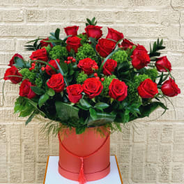 Red roses arranged in a round box with green filler and foliage