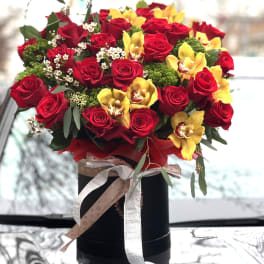 Bouquet of red roses and yellow orchids in a black box with ribbon
