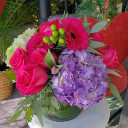 Bouquet of pink roses, purple hydrangea, and magenta gerbera daisies in a glass vase