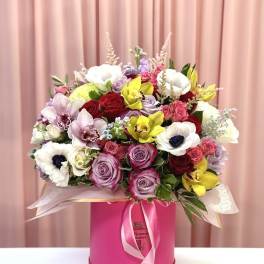 Mixed bouquet of roses, orchids, and anemones in a pink hat box