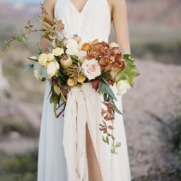 Bride holding a cascading bouquet of cream, peach, and rust flowers