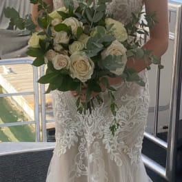 Bride holding a hand-tied bouquet of ivory roses with abundant greenery