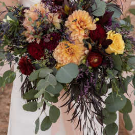 Bride holding a bouquet of peach, red, and yellow flowers with eucalyptus