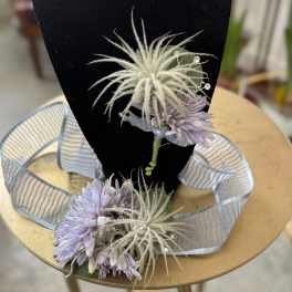 Lavender corsage with ribbon and white feathery accents on a black display stand