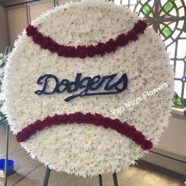 Large round baseball-shaped wreath of white flowers with red seams and blue Dodgers script on an easel.