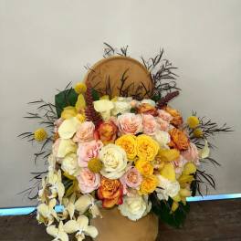 Large bouquet of roses and orchids in a tan hatbox