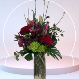 Bouquet of red roses, pink lilies, and green hydrangea in a tall glass vase