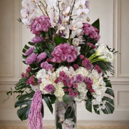 Tall floral arrangement with pink roses, white orchids, and hydrangeas in a glass vase