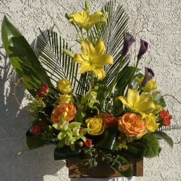 Tall arrangement of yellow lilies, orange and yellow roses, and green orchids in a wooden box