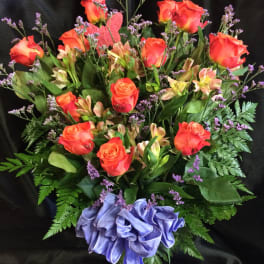 Orange roses and alstroemeria in a glass vase with a purple ribbon