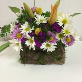Mixed bouquet of daisies, lilies, and purple blooms in a burlap-wrapped container