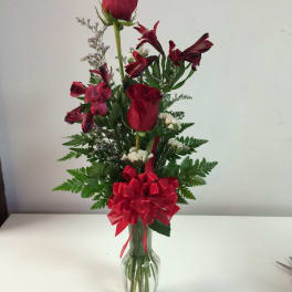 Red roses and burgundy flowers in a clear glass vase with a red bow