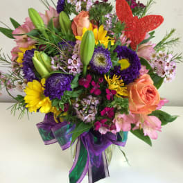 Colorful mixed bouquet in a clear glass vase with a red butterfly pick