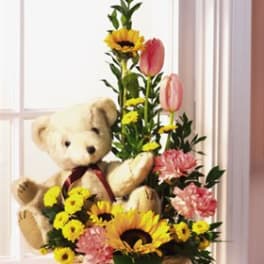 Teddy bear in a basket with sunflowers, tulips, and pink flowers