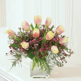 Arrangement of pale yellow and pink tulips with small purple blooms in a clear glass vase