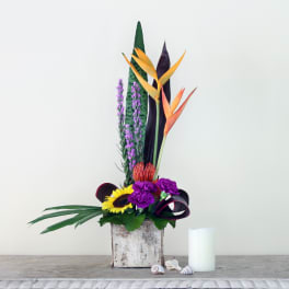 Tropical flower arrangement in a rustic wooden container with a white candle