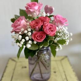 Pink roses in a glass jar with baby's breath and a glittery heart pick