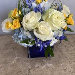 Blue and white floral arrangement with yellow roses in a cobalt vase