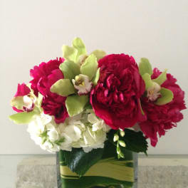 Bouquet of red peonies, white hydrangeas, and green orchids in a glass vase